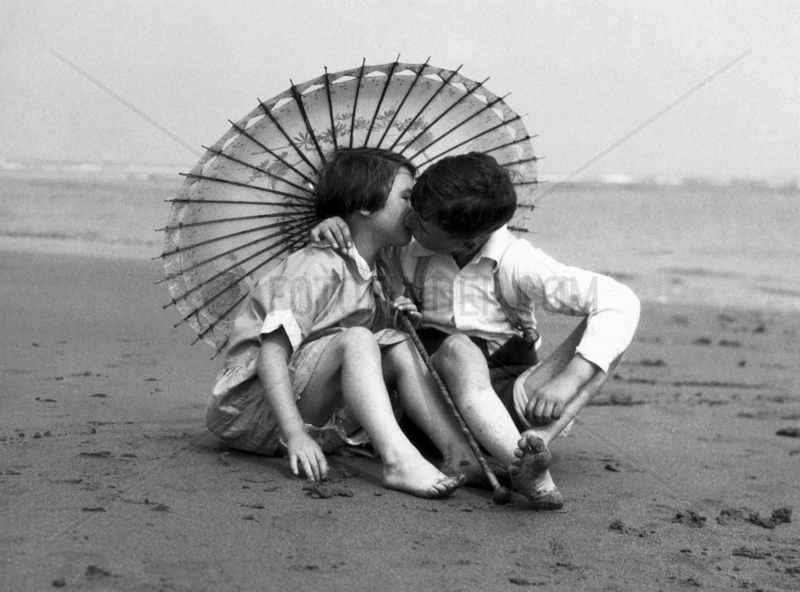 Girl and boy kissing under a parasol,  c 1930s.