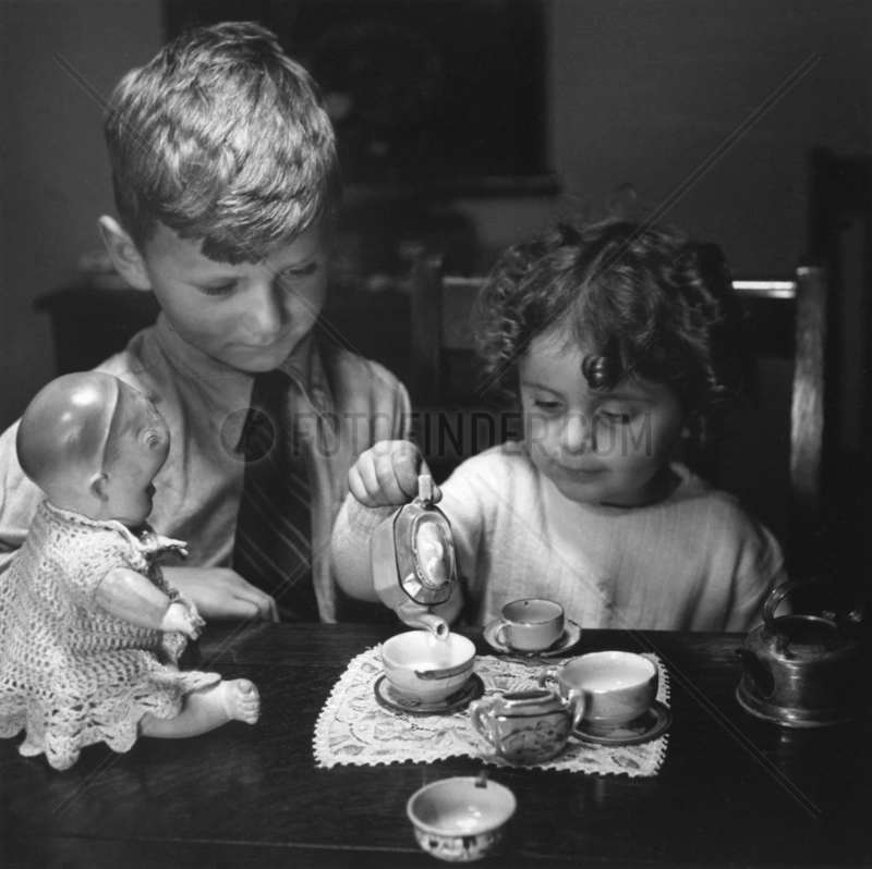 Little girl pouring tea as her brother looks on,  c 1930s.
