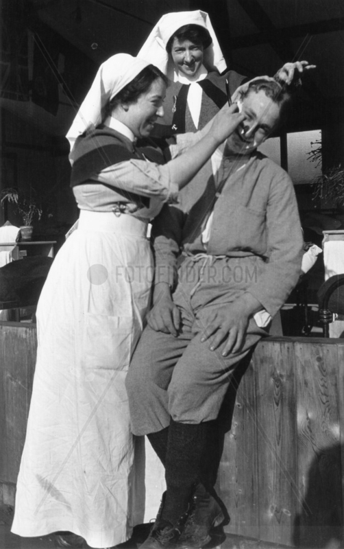 Nurse shaving a soldier with another nurse in close attendance,  c 1910s.