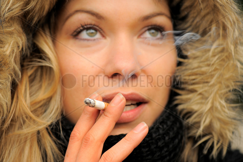 Junge Frau raucht eine Zigarette im Abendlicht,  Schaerfe auf Hand.