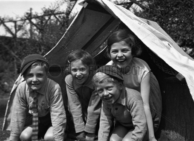 Four children smiling from the entrance of a tent,  c 1920s.
