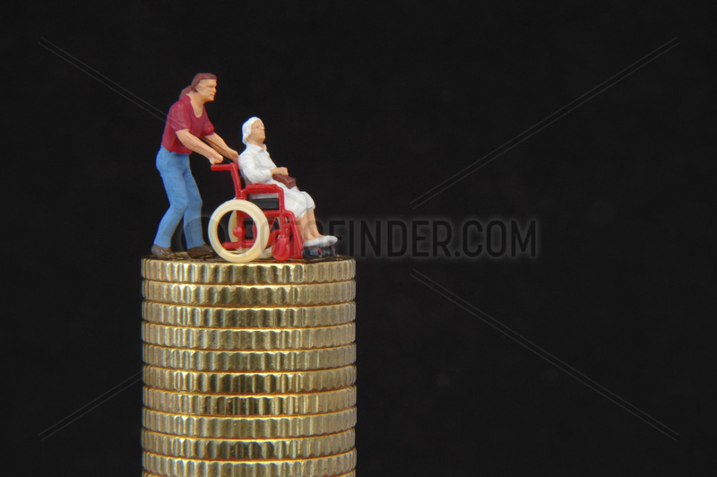Figur im Rollstuhl steht auf einem Stapel Muenzen
