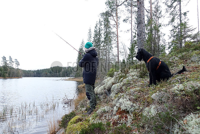 Braenna,  Schweden,  Junge angelt in Begleitung seines Hundes an einem See