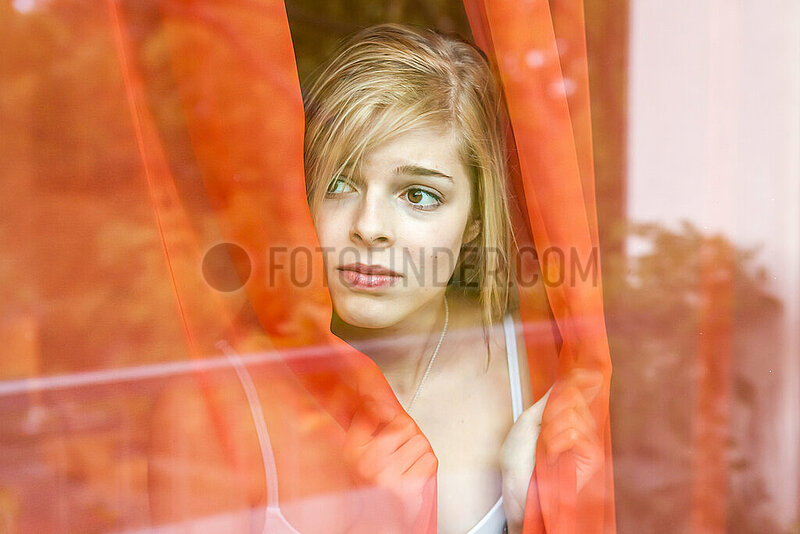 junge Frau am Fenster blickt aengstlich nach draussen