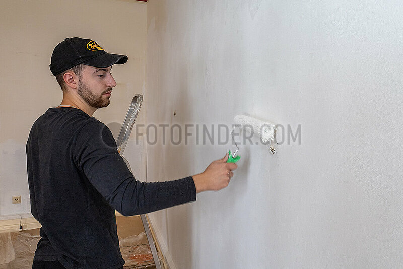 junge Mann streicht Zimmerwand