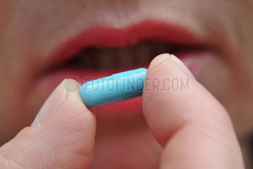 blaue Kapsel in den Fingern vor dem Mund