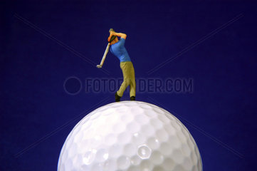 kleine Figur eines Golfers macht einen Abschlag auf einem Golfball