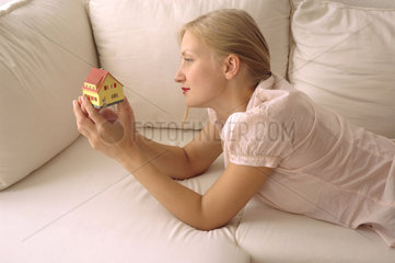 junge Frau traeumt schaut auf Miniaturhaus