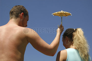 Mann haelt kleinen Sonnenschirm ueber Frau
