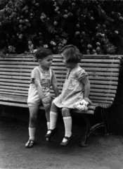 Junge und Maedchen sitzen auf Bank 1930