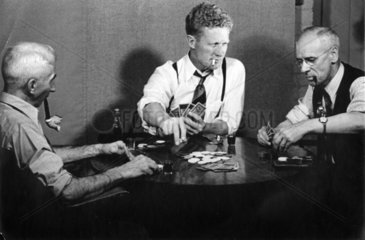 drei rauchende Maenner spielen Karten