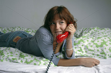 Frau telefoniert auf Bett liegend