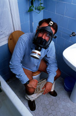 Mann sitzt mit Gasmaske auf Toilette