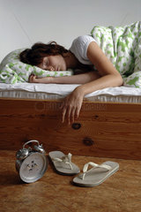 Frau mit Flip-Flops und Wecker neben dem Bett