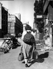 Frau mit Rucksack und Taschen an Blumenstand im zerstoerten Berlin