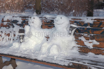 zwei Schneemaenner auf einer Parkbank