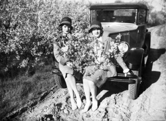 Zwei Frauen sitzen mit Blumen auf einem Auto