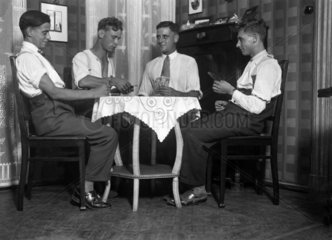 vier junge Maenner beim Kartenspielen an einem Tisch