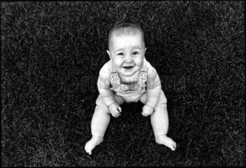 Baby sitzt lachend auf einer Wiese