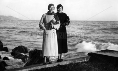 zwei Frauen in Maenteln posieren am der Kueste