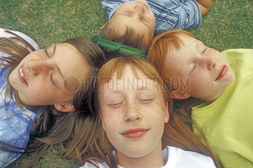 vier Kinder liegen Kopf an Kopf mit geschlossenen Augen