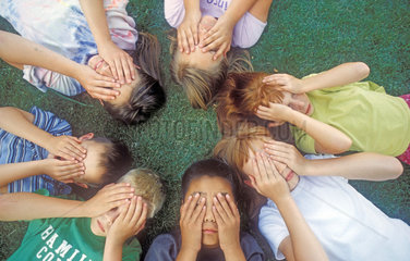 sieben liegende Kinder halten sich die Augen zu