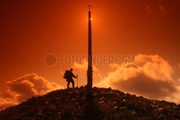 Pilger neben Gipfelkreuz bei Sonnenuntergang am Jakobsweg - Camino de Santiago