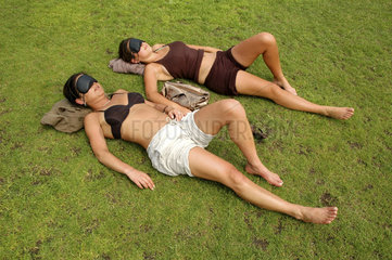 zwei Frauen sonnen sich im Gras mit Schlafmasken als Sonnenschutz
