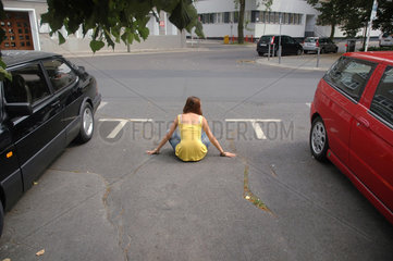 Frau sitzt auf leerem Parkplatz zwischen zwei Autos