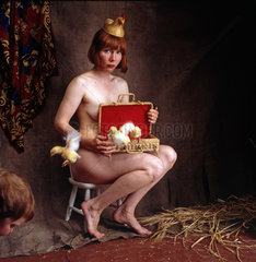 nackte Frau posiert mit Huehnerhut und zwei Kueken