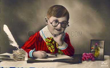kleiner Junge mit bunter Kleidung sitzt an Schreibtisch und schreibt Liebesbrief