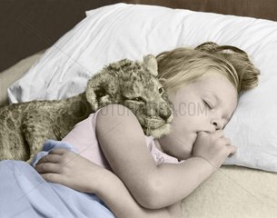 Maedchen schlaeft mit Loewenbaby in einem Bett