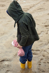 Hamburg  Kind mit Regenjacke und Gummistiefeln steht in einer Pfuetze