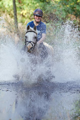 Zernikow  Frau reitet auf ihrem Pferd im Galopp durch einen See