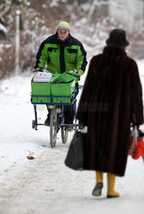 Berlin  Deutschland  Postbote der PIN AG faehrt auf seinem Fahrrad einen schneebedeckten Gehweg entlang