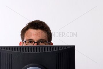 Freiburg  Deutschland  Mann mit Brille sitzt hinter einem Computermonitor
