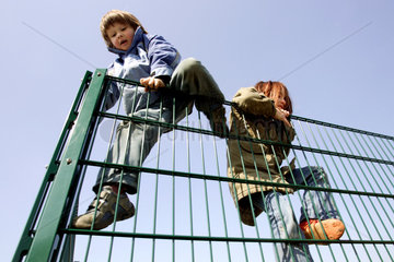 Werl  Junge und Maedchen klettern ueber einen Zaun