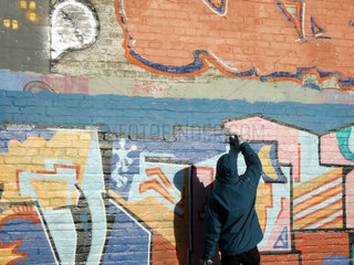 Berlin  Deutschland  Jugendlicher in Kapuzenjacke sprueht ein Graffito an eine Wand