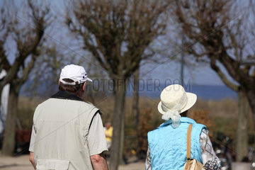 Touristen mit Sonnenhueten vor Baeumen ohne Laub in Ahlbeck an der Ostsee