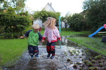Handewitt  Deutschland  ein Junge und ein Maedchen laufen in Gummistiefeln durch einen ueberschwemmten Garten