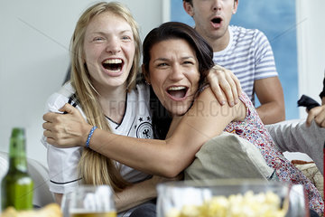 Football enthusiasts embracing and smiling happily while watching match at home