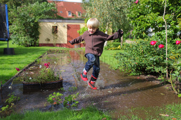 Handewitt  Deutschland  ein Junge laeuft in Gummistiefeln durch einen ueberschwemmten Garten