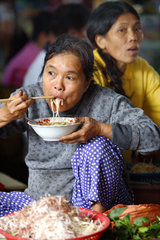 Vietnam  Marktfrau isst ein asiatisches Nudel-Gericht mit Staebchen