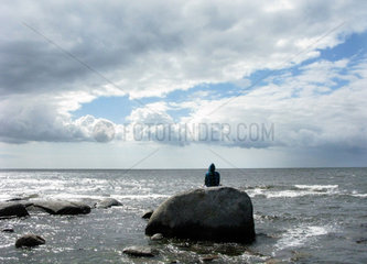 Karlskrona  Schweden  Tourist sitzt auf einem Felsen an der Kueste