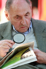 Koeln  Deutschland  alter Mann liest seine Zeitung mit Hilfe einer Lupe