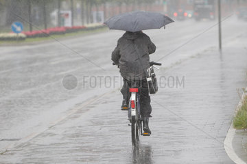 Kiel  Deutschland  eine Radfahrerin faehrt bei starkem Regen mit einem Regenschirm
