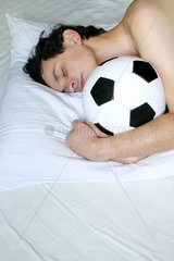 Berlin  Deutschland  Mann liegt mit Fussball im Bett