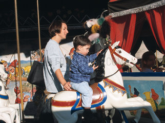 Mutter mit Sohn  der auf einem Karusselpferd sitzt