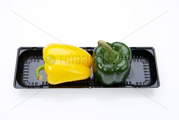 Eine gelbe und eine gruene Paprikaschote liegen in einer Kunststoffschale