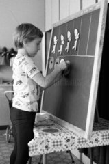 Berlin  DDR  Junge klebt in der Vorschule Figuren aus Papier an eine Tafel